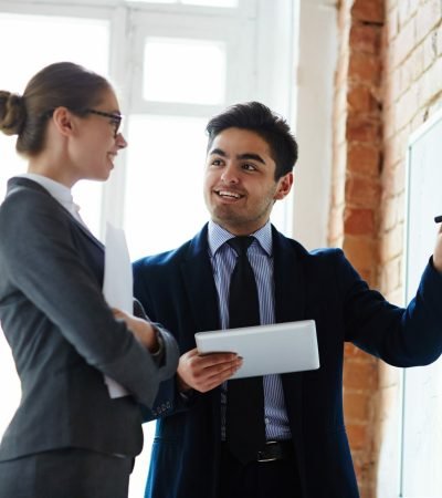 Young economist pointing at whiteboard while explaining statistics to colleague